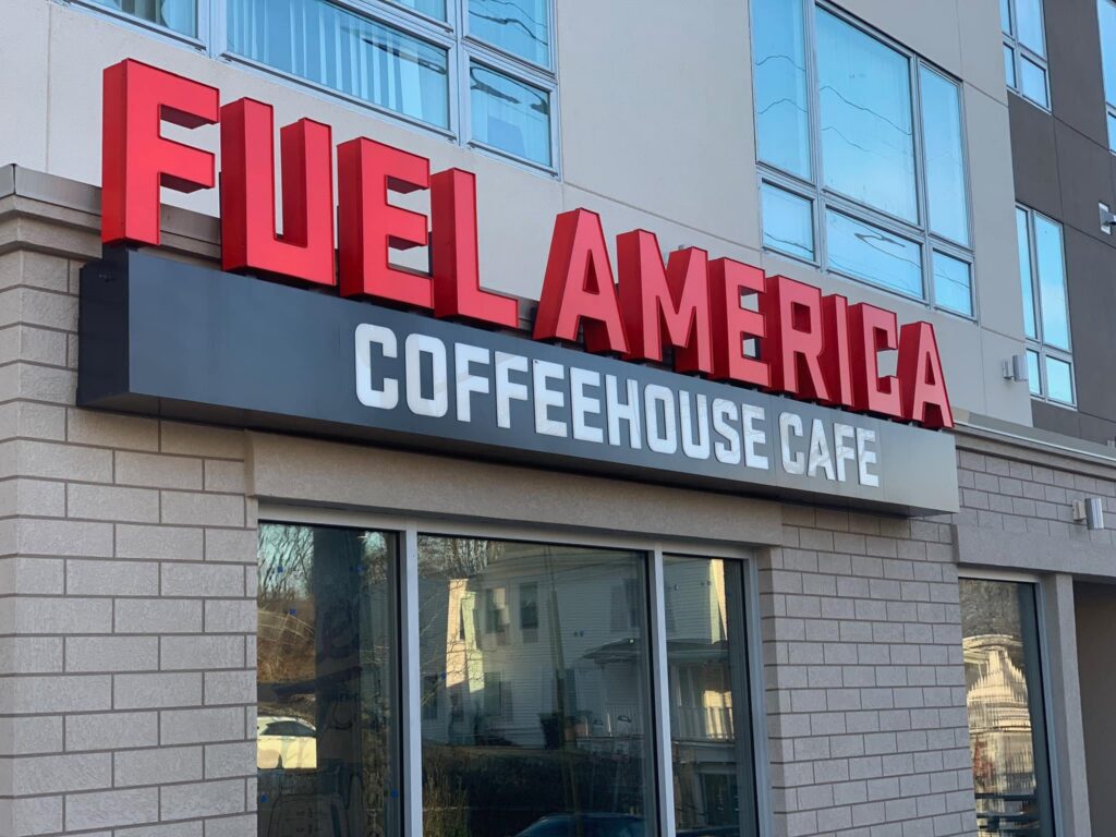 The Weymouth Fuel America location, specifically its sign in red, black, and white. It reads Fuel America, with the words coffeehouse cafe underneath.